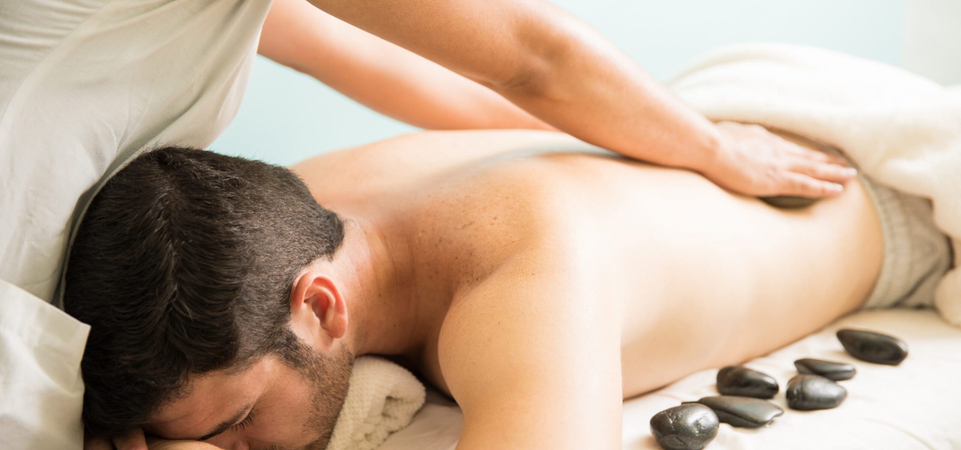 Closeup of a female therapist giving a hot stone massage to a young man in a spa